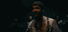 a man in a white shirt and suspenders is standing in a dark room with his hands outstretched .