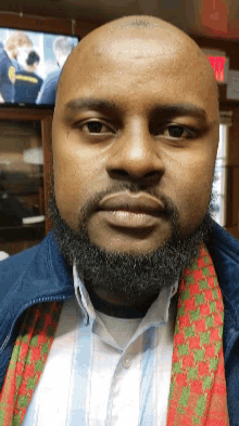 a bald man with a beard and a scarf around his neck looks at the camera