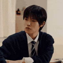 a young man wearing a cardigan and tie is sitting at a desk .