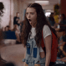 a girl wearing overalls and a red backpack with a netflix logo on the bottom