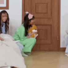 a woman in a green shirt is kneeling down in front of a wooden door holding a stuffed animal .