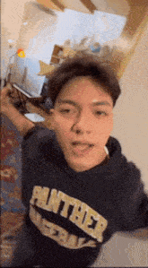 a young man wearing a panther sweatshirt is taking a selfie .