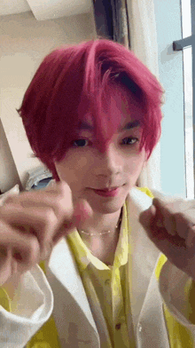 a young man with pink hair and a yellow shirt is making a heart with his hands .