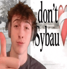 a man wearing headphones giving a thumbs up in front of a sign that says " do n't sybau "