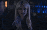 a woman with blonde hair is standing in a dark room with blue lights behind her