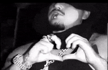 a black and white photo of a man making a heart with his hands