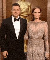 a man in a tuxedo and a woman in a dress pose for a picture in front of an oscar statue