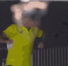 a blurry picture of a man in a yellow shirt standing in front of a fence .