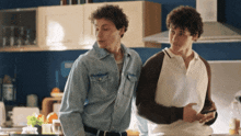 two men are standing in a kitchen and one of them is looking at his phone