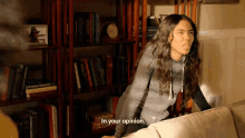 a woman sitting on a couch with a bookshelf behind her that says in your opinion