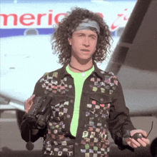 a man with curly hair is holding a video camera in front of an american airlines sign