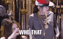 a woman wearing a hat and gold chains says who that