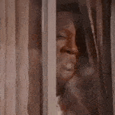 a woman is peeking out of a window with her eyes closed and smiling .