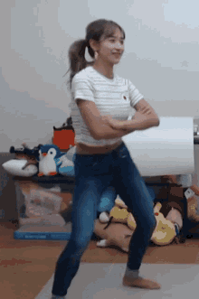a woman in a striped t-shirt and jeans is dancing in a room with stuffed animals .