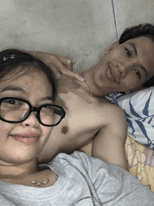 a woman wearing glasses is laying next to a shirtless man on a bed