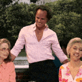 a man in a pink shirt smiles while standing next to two women