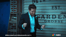 a man in a suit stands in front of a sign that says " garden grosse "