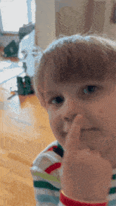 a young boy holds his finger to his nose and looks at the camera
