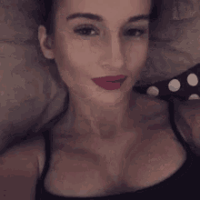 a woman in a black tank top is taking a selfie while laying on a bed .