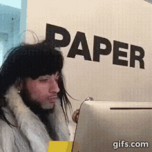 a man in a fur coat is standing in front of a wall with the word paper on it