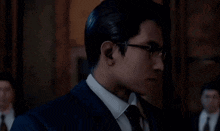 a man wearing glasses and a suit points his finger at the camera