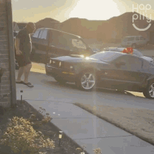 a man walks down a sidewalk next to a mustang and a truck with the word hop on the bottom