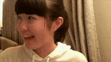 a girl in a white sweatshirt is smiling in front of a window