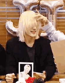 a man with long blonde hair is sitting at a table holding a picture of a man .
