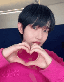 a young man in a pink shirt is making a heart shape with his hands
