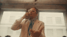 a man wearing a white suit and glasses is talking on a phone