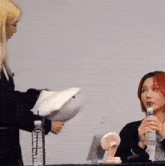 a woman is holding a stuffed animal while another woman drinks water