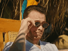 a man wearing sunglasses is sitting in a chair with a parrot on his head