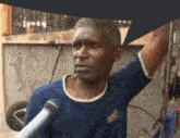 a man is talking into a microphone while wearing a blue shirt