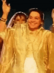 a woman in a yellow dress is smiling and waving her hand