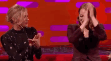 two women are sitting next to each other on a stage and clapping their hands .