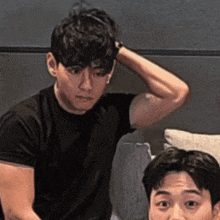 a man in a black shirt is sitting next to another man with his hand on his head