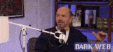 a man sitting in front of a microphone with the words dark web on the bottom right