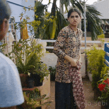 a woman is standing in front of a bunch of potted plants and the name sanjo_sebi is on the bottom right