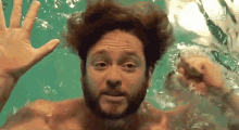a man with a beard is swimming underwater and reaching for the camera