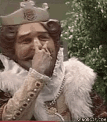 a man in a king costume is covering his mouth with his hand while smoking a cigarette .