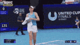 a woman walking on a tennis court in front of a united cup finals sydney sign
