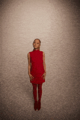 a woman in a red dress is standing in front of a white wall