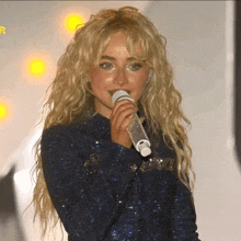 a blonde woman singing into a microphone with the letter r visible in the corner