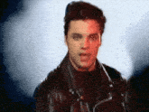 a man wearing a black leather jacket is standing in front of a blue background