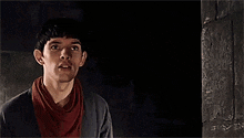 a man with a scarf around his neck is standing in a dark room looking up .