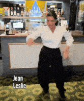 a woman in a white shirt and black pants is dancing in front of a bar with the name jean leslie above her