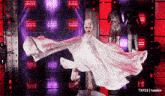 a drag queen in a white dress is dancing on a stage