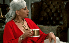 a woman in a red top is holding a gold cup of coffee