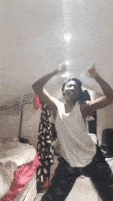 a young man in a white tank top is dancing in a bedroom