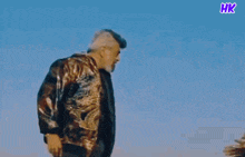 two men standing next to each other with a blue sky in the background and a hk logo